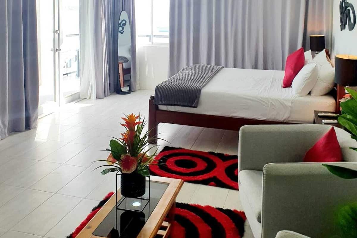 A hotel room with a bed, a desk, a chair, a plant, and a ceiling fan.