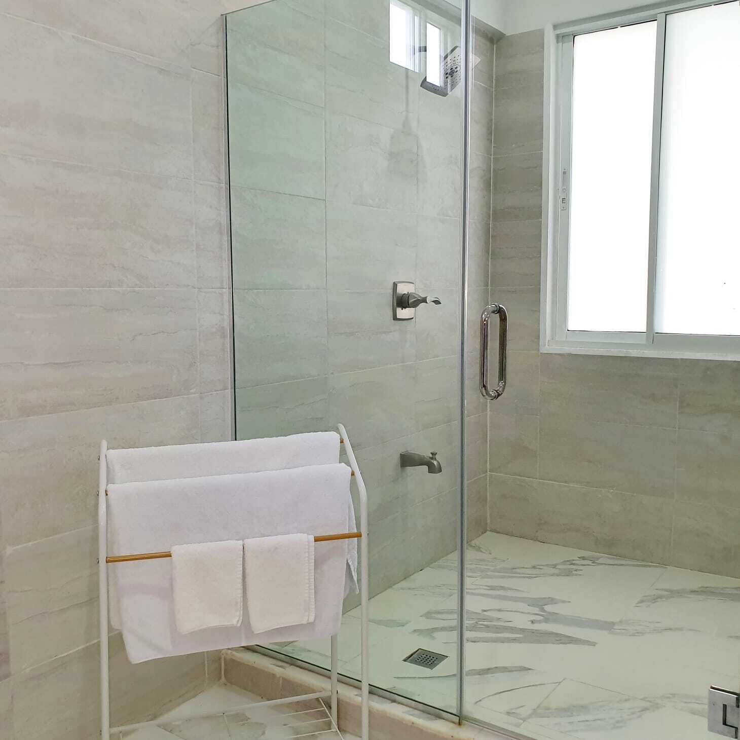 A glass-enclosed shower with a white towel rack, a glass door, and a window with blinds.