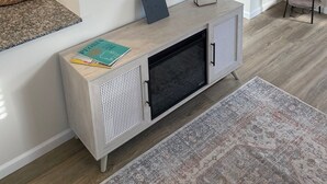 A living room with a flat-screen TV mounted on the wall, a small console table with a clock, and a floor lamp.
