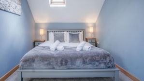 A neatly made bed with a grey duvet, two bedside lamps, and a small bedside table with a lamp. - Tor Bay Cottage - 1 Bedroom - Parkmill (Swansea)