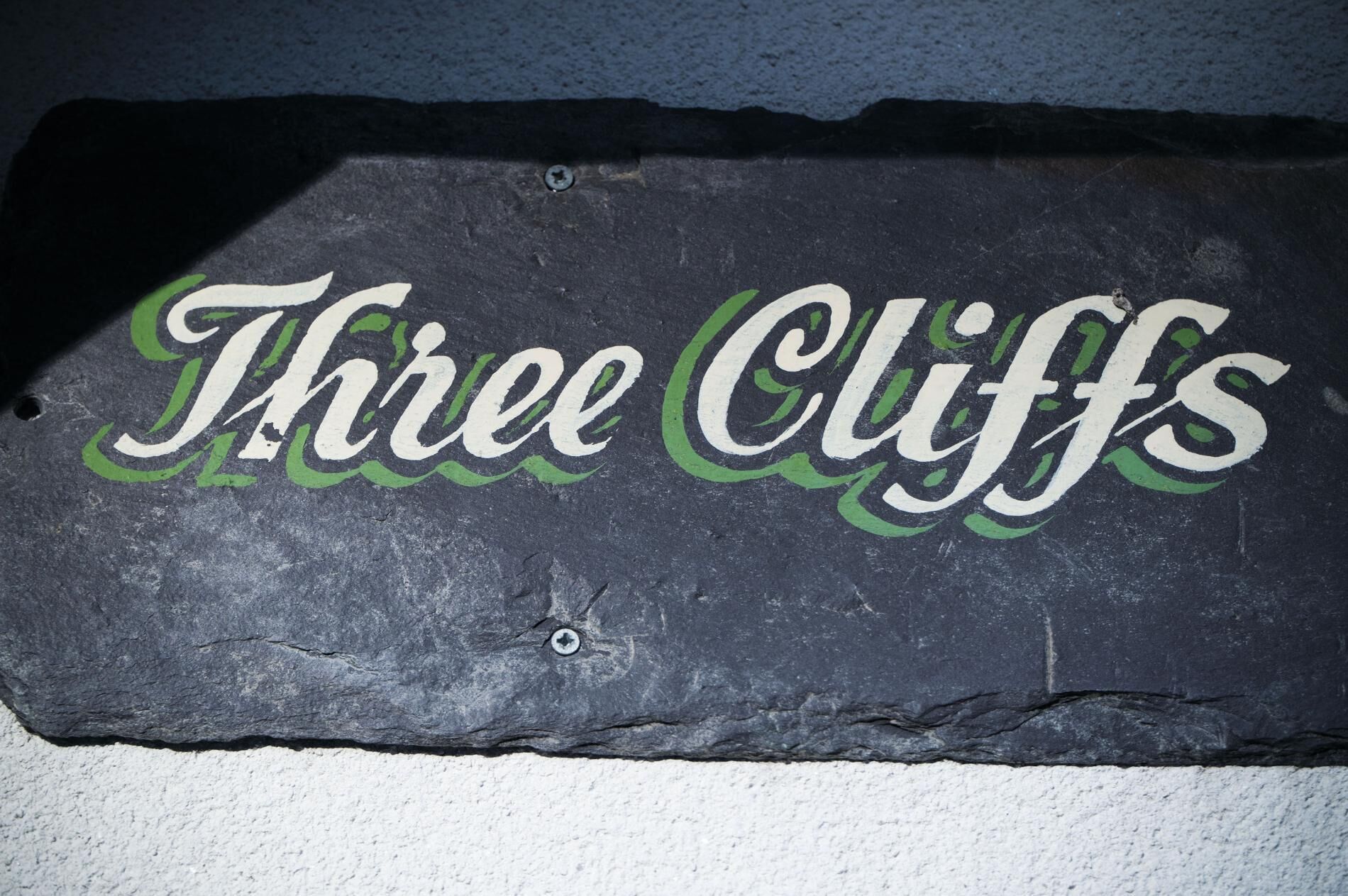 Un cartel de pizarra con el texto 'Three Cliffs' en letras estilizadas.