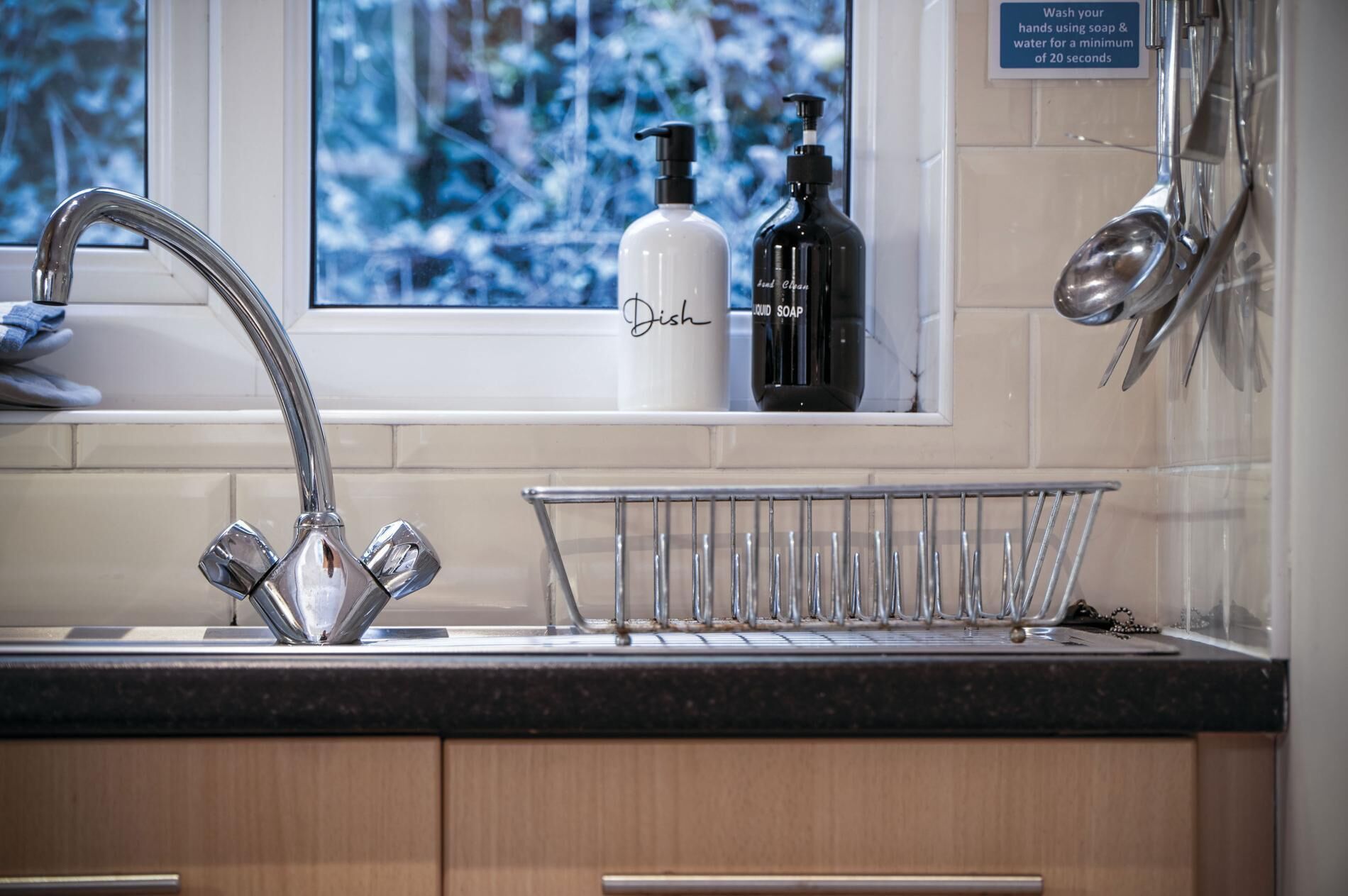 A kitchen with a stainless steel sink, a dish rack, and two soap dispensers on the counter.