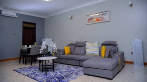 A living room with a gray sofa, a small round table, and a blue patterned rug. - Malaikanzi Apartments (Namulanda)