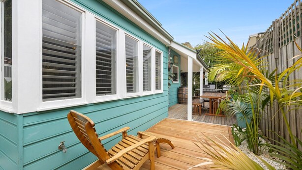 A turquoise house with a wooden deck, a wooden chair, and a patio area with a grill and plants. - Price on the Beach 2c Pet-Friendly Steps to Beach (Torquay)