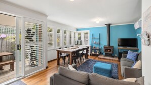 A cozy living room with a fireplace, a TV, and a dining area with a table and chairs. - Price on the Beach 2c Pet-Friendly Steps to Beach (Torquay)