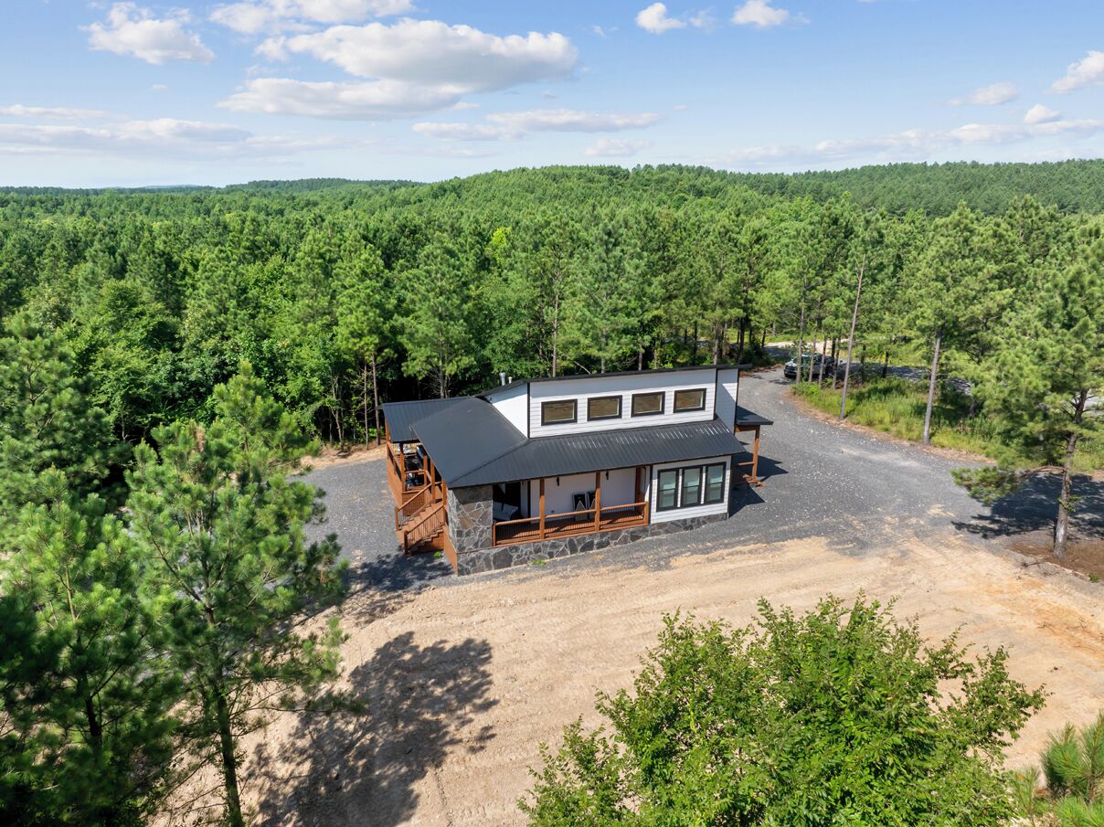 A two-story cabin with a stone foundation, large windows, and a covered porch.