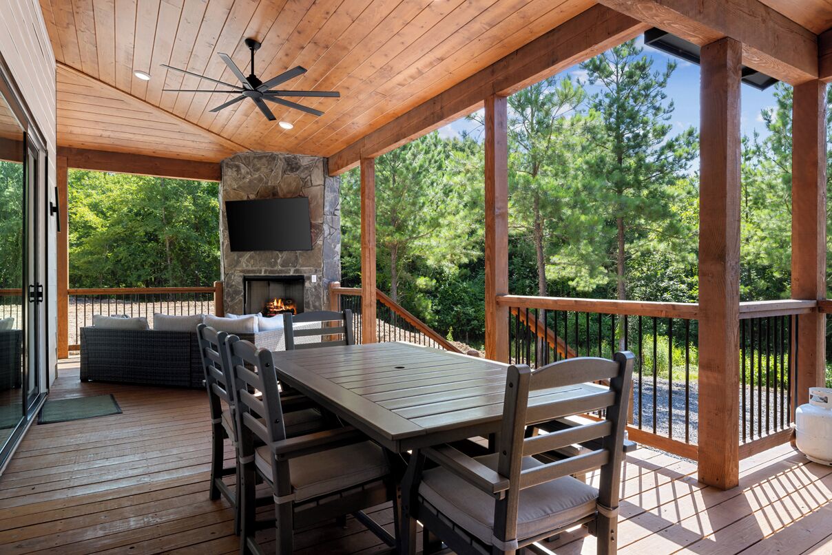 A covered outdoor area with a stone fireplace, wooden deck, and a TV mounted on the wall.