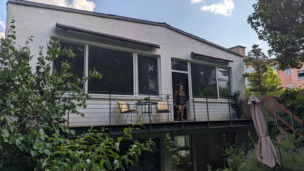 Ett tvåvåningshus med stora fönster, en balkong och en trädgård.