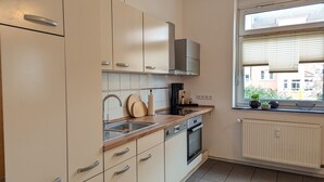 Ett modernt kök med beige skåp, en diskho i rostfritt stål och ett fönster med persienner.