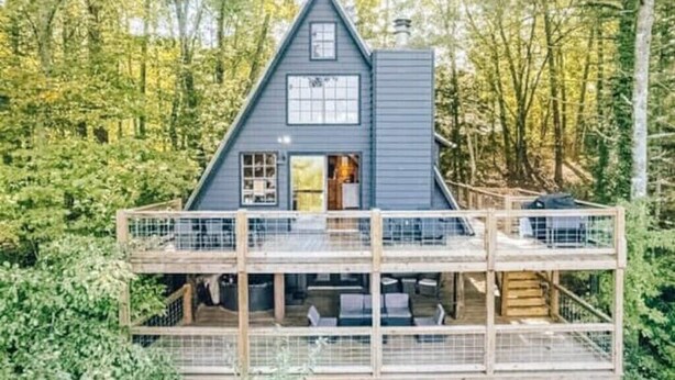 Una cabaña con terraza de madera y balcón, rodeada de árboles.