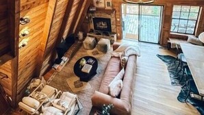 Una habitación acogedora en el ático con paredes de madera, una chimenea de piedra, un sofá y una mesa de comedor.