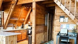 Un loft espacioso con techo alto, vigas de madera, zona de cocina, comedor y una escalera.