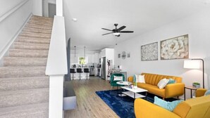 Ein modernes Apartment mit Treppe, einem Wohnzimmer mit gelbem Sofa, einem Essbereich und einer Küche.