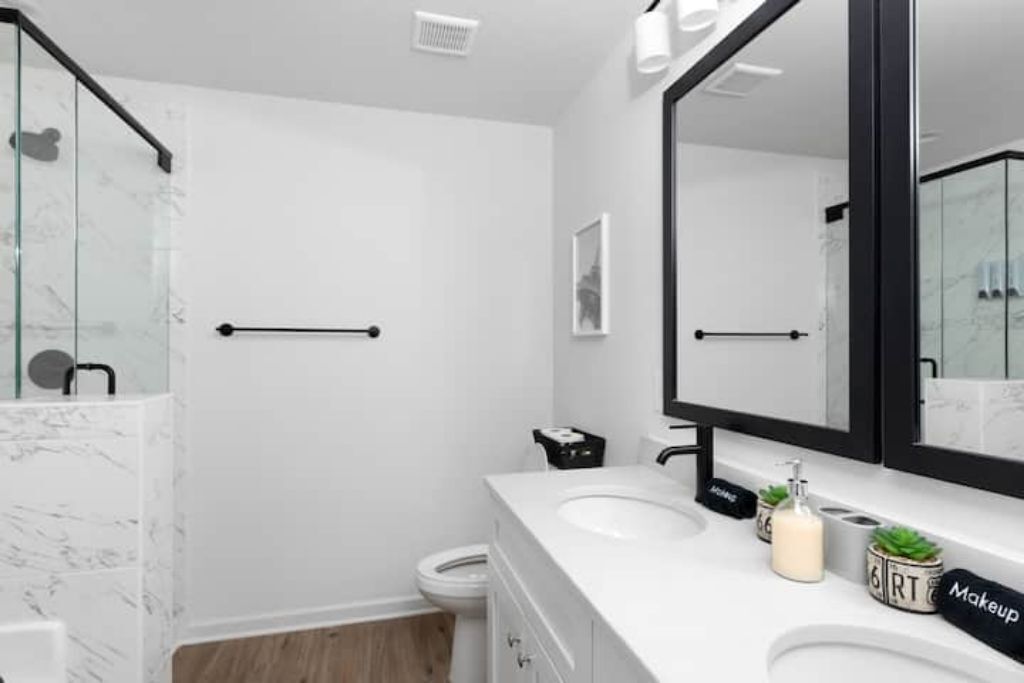 Un bagno moderno con una parete in marmo bianco, uno specchio grande e un lavandino bianco.