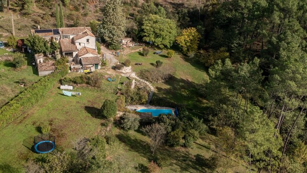 Ein Wohnhaus mit Swimmingpool, Trampolin und großem Gebäude, umgeben von Bäumen und einer hügeligen Landschaft.