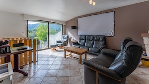 Ein Wohnzimmer mit einem schwarzen Ledersofa, einem Holztisch und einem großen Fenster mit Blick auf Grünflächen.