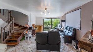 Ein geräumiger Wohnbereich mit Treppe, einem Ledersofa, einem Holztisch und einem großen Fenster mit Blick auf Grünflächen.