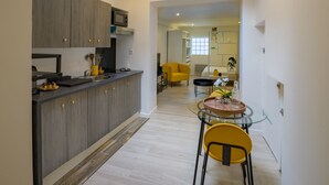 Una cocina moderna con armarios grises, un microondas y un comedor con mesa de vidrio y sillas amarillas.
