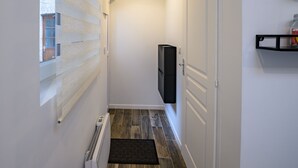 Un pasillo estrecho con piso de madera, un radiador, un felpudo negro, un televisor montado en la pared y una puerta con marco blanco.