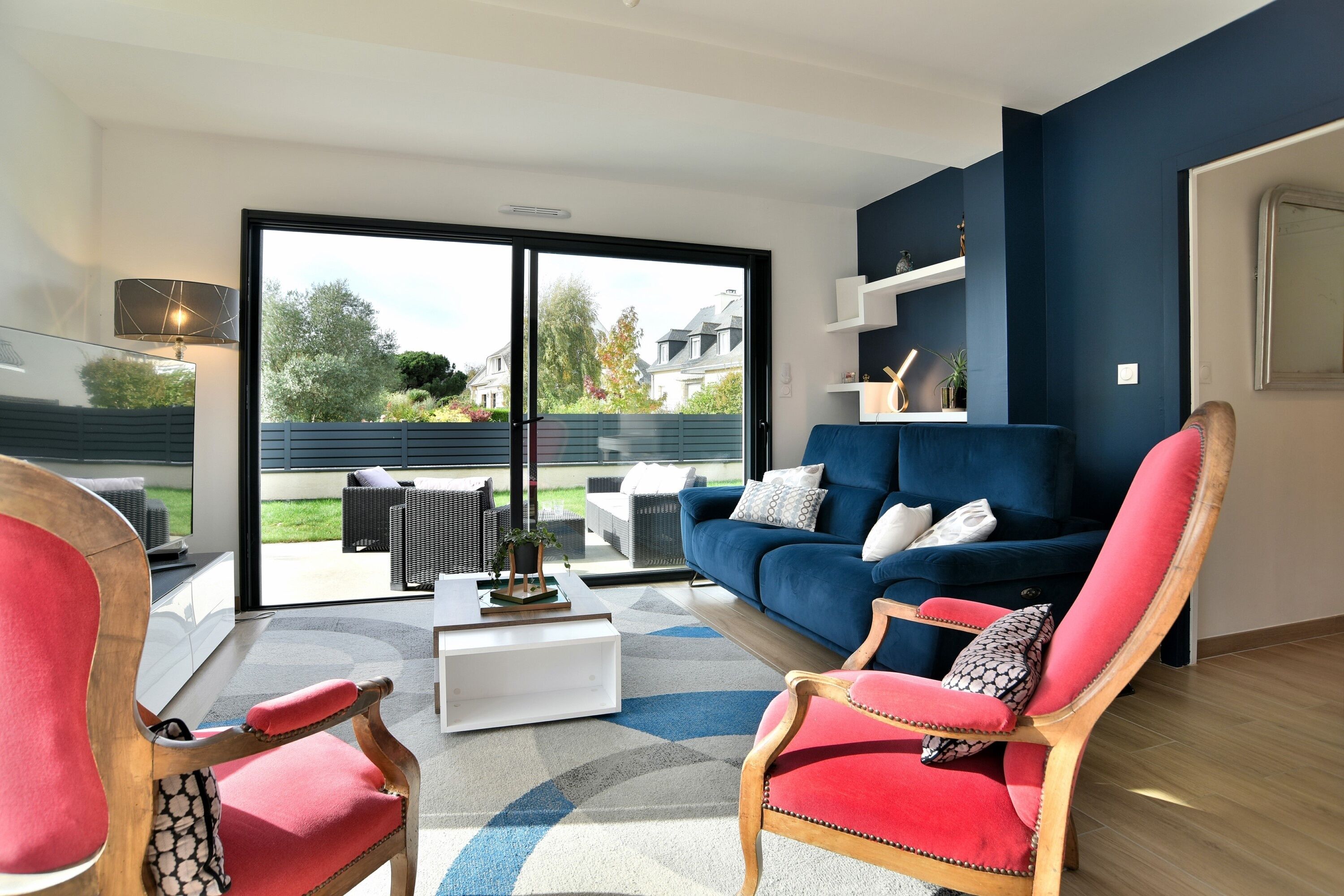 A modern living room with a blue sofa, red armchairs, and a white coffee table.