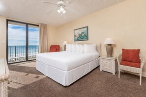 A hotel room with a large bed, a balcony with a view of the beach, a ceiling fan, and a painting on the wall. - Phoenix X 317 - Gulf Front Condo (Orange Beach)