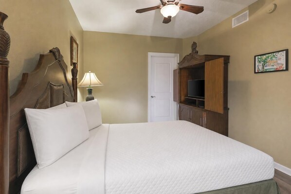 A hotel room with a bed, a ceiling fan, a television, and a door.