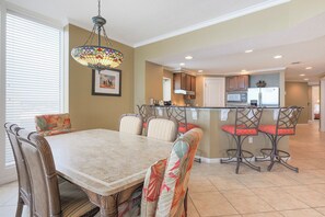 A dining area with a marble table and wicker chairs, a kitchen with a refrigerator and stove, and a bar area with stools.