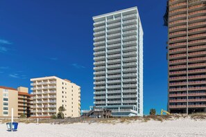 Un grand hôtel moderne doté de nombreux balcons, situé sur une plage de sable et entouré d’autres bâtiments.