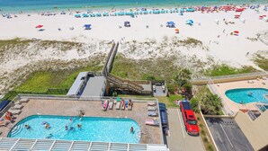 A beach resort with a pool area, beach umbrellas, and a staircase leading to a deck. - Colonnades 803 - Spacious Gulf Front Condo (Gulf Shores)