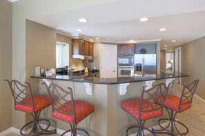 A kitchen with a central island, stainless steel appliances, and red patterned chairs.