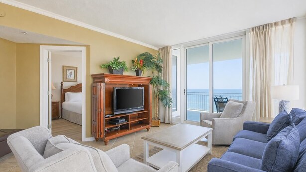 Una habitación de hotel con balcón, televisor, sofá y sillón.