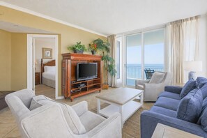 A hotel room with a balcony, a TV stand, a sofa, and a chair.