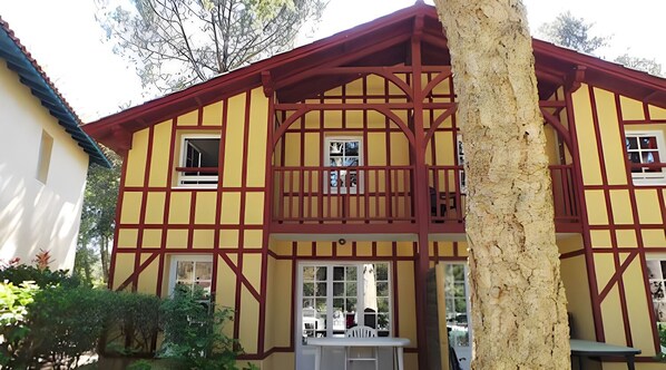 A traditional half-timbered house with a balcony, a small garden, and a white door.