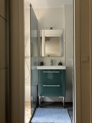 A bathroom with a glass shower enclosure, a white sink, and a green vanity with two drawers.