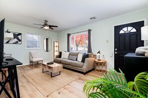 A living room with a sofa, a coffee table, a chair, a TV, a ceiling fan, a window with curtains, a door, and a plant. - "TheGem" by ForestPark, TheHill & HospitalCorridor (St Louis)