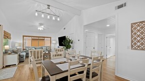 A spacious living area with a dining table, chairs, and a sofa. There is a TV and a plant in the room.