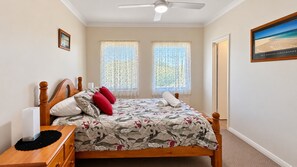 A bedroom with a wooden bed, floral bedding, two windows with sheer curtains, a ceiling fan, and a framed picture on the wall. - Central on Kent Busselton (Busselton)