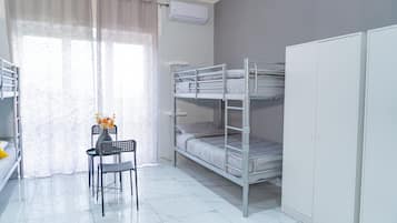 Ein Schlafsaalzimmer mit Etagenbetten, einem Schreibtisch mit Stuhl, einer Vase mit Blumen und einem Kleiderschrank.