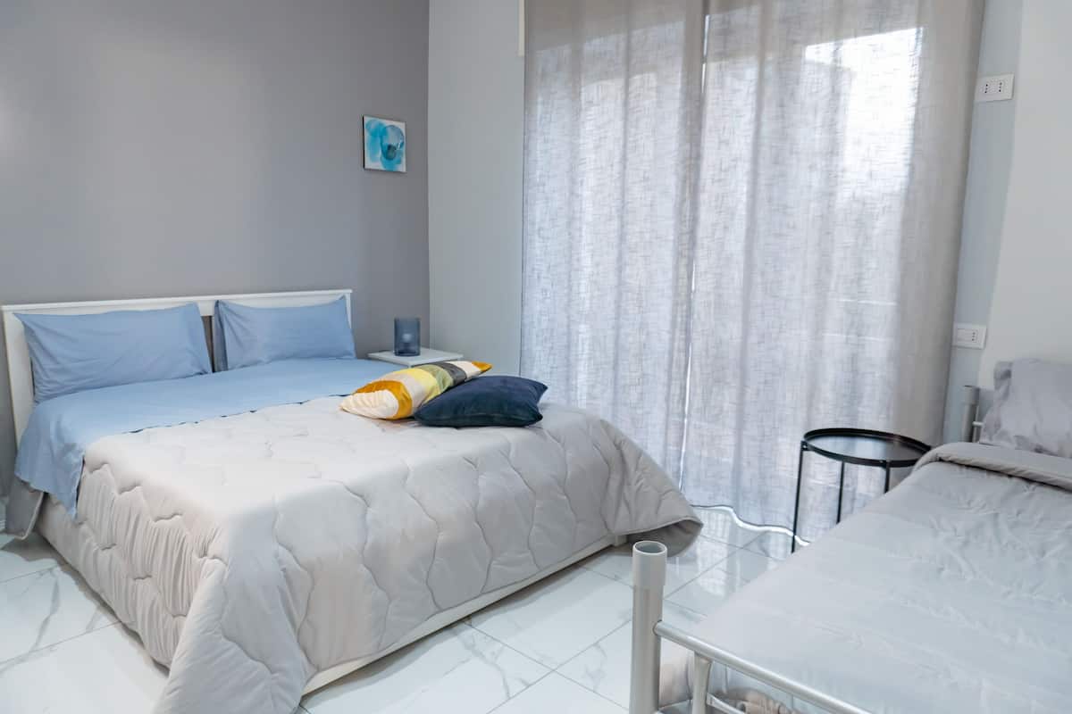 A bedroom with a bed, a bedside table, a lamp, and a window with curtains.