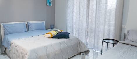 Un dormitorio con cama, mesita de noche, lámpara y ventana con cortinas.