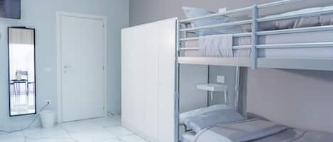 A bunk bed room with a white wardrobe, a chair, and a small table.