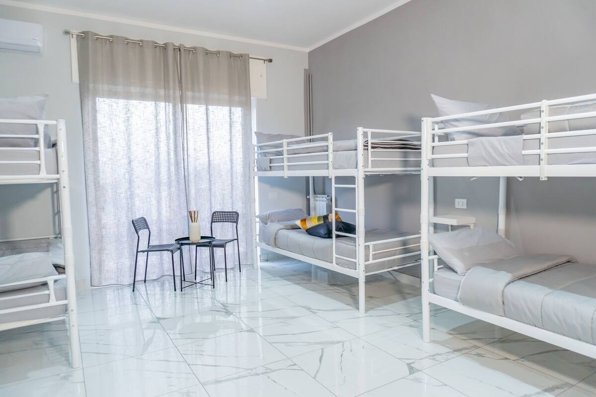A bunk bed room with a table and chairs, a window with curtains, and a tiled floor.