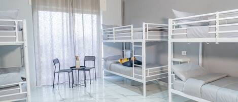 A bunk bed room with a table and chairs, a window with curtains, and a tiled floor.