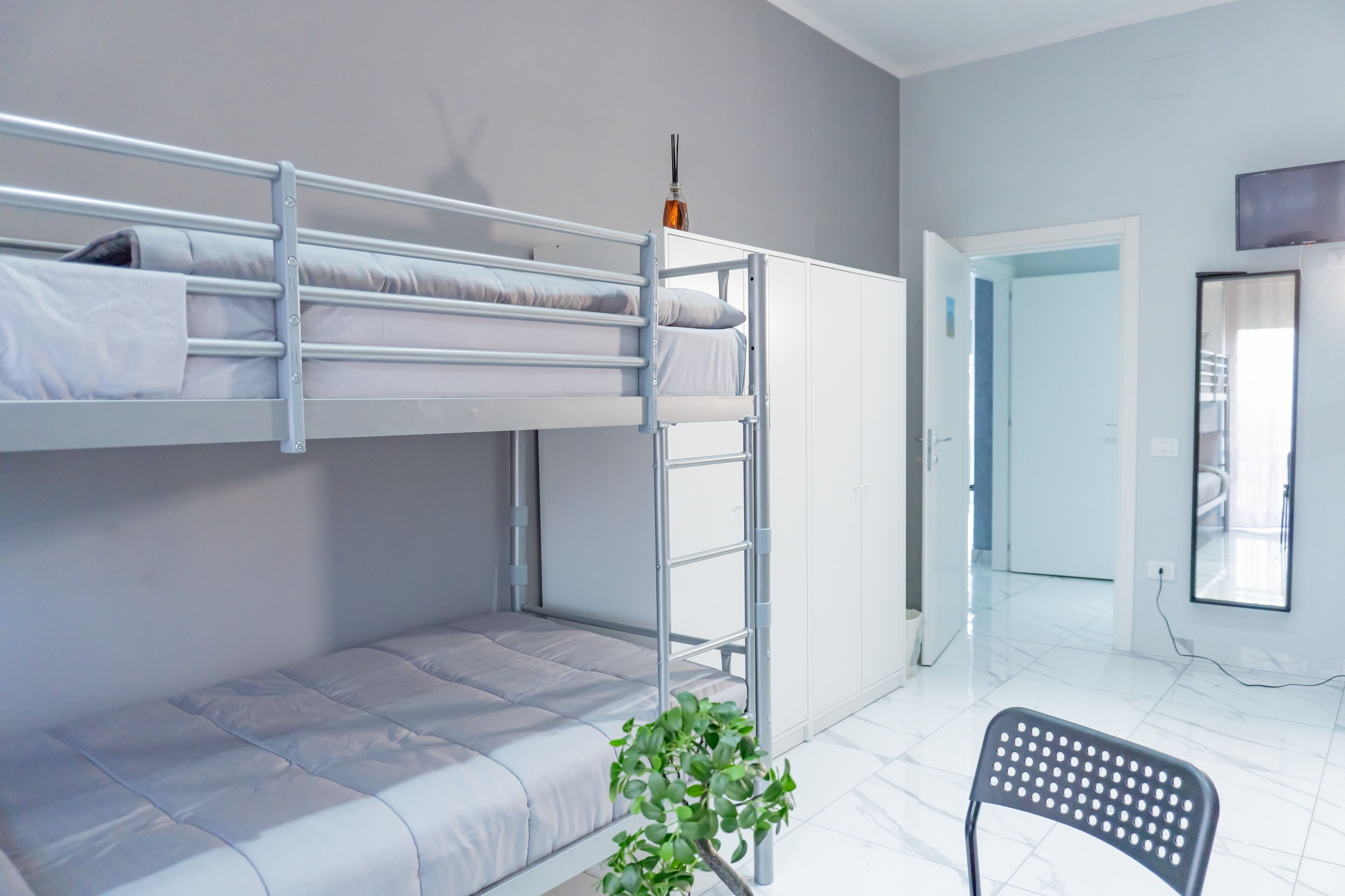 A bunk bed room with a ladder, a chair, and a potted plant.