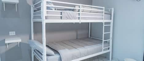 A bunk bed with a white frame, a small shelf, and a white bucket on the floor.