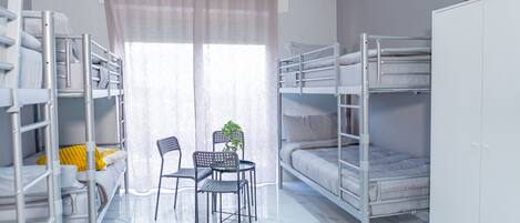 A dormitory room with bunk beds, a small table, chairs, and a potted plant.