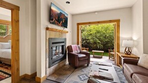 A cozy living room with a fireplace, a comfortable sofa, a leather armchair, and a view of greenery outside. - Ski Side Retreat: Soak, Ski, Sip (Telluride)