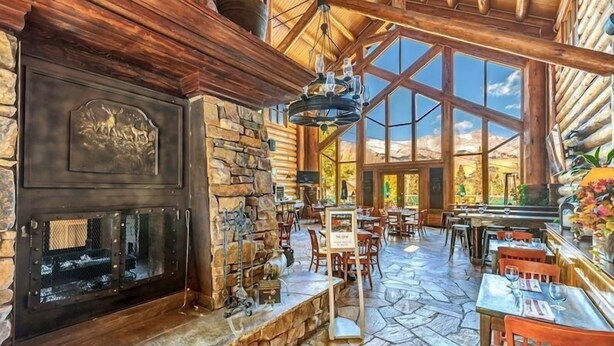 A spacious lodge with a stone fireplace, wooden beams, and large windows offering views of the outdoors. - Ski Side Retreat: Soak, Ski, Sip (Telluride)