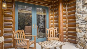A log cabin with a stone wall, a wooden door, and two wooden chairs and a table outside. - Ski Side Retreat: Soak, Ski, Sip (Telluride)