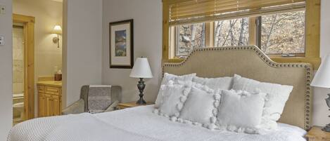 Una camera da letto con un letto grande, una testiera in legno, una finestra con persiane, un comodino con una lampada e una sedia.